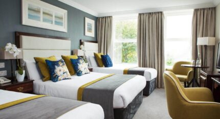 Elegant hotel room with three cosy beds, plush seating, and large window views.