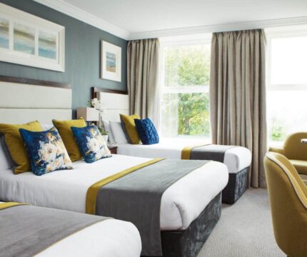 Elegant hotel room with three cosy beds, plush seating, and large window views.