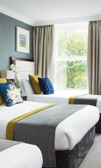 Elegant hotel room with three cosy beds, plush seating, and large window views.