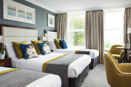 Elegant hotel room with three beds, soft lighting, and garden view through large window.
