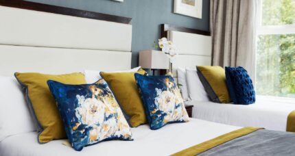 Elegant hotel room with twin beds, colourful cushions, and a bright window view.