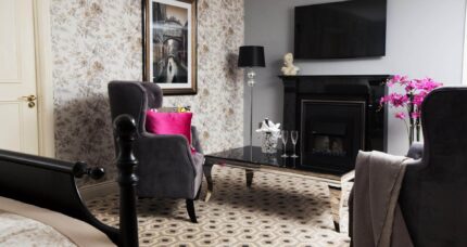 Elegant hotel room with plush chairs, a cosy fireplace, and floral decor at The Anner Hotel.
