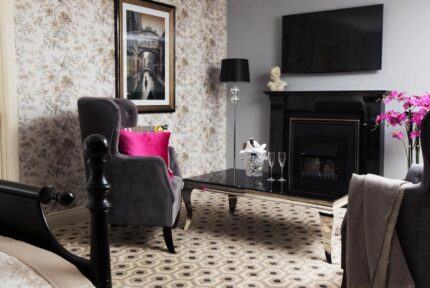 Elegant hotel room with plush chairs, a cosy fireplace, and floral decor at The Anner Hotel.