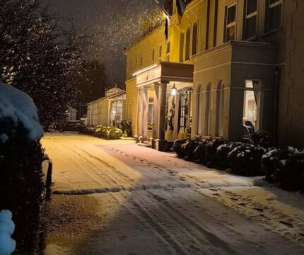Snowy evening at The Anner Hotel entrance, lit warmly, inviting for family stays.