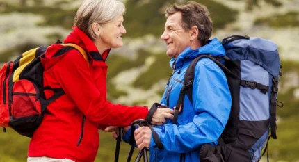 Mature couple hiking in scenic mountain landscape, smiling in colourful jackets and backpacks.