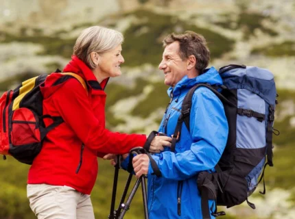 Mature couple hiking in scenic mountain landscape, smiling in colourful jackets and backpacks.
