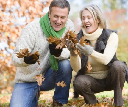 A smiling couple enjoying autumn leaves in a park, wearing cosy jumpers and scarves.